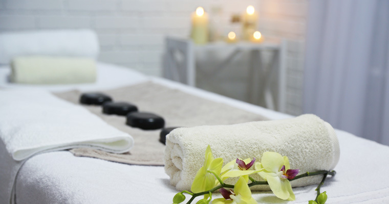 Bild eines Massageraumes mit Kerzen, einer Massageliege und Massage-Steinen